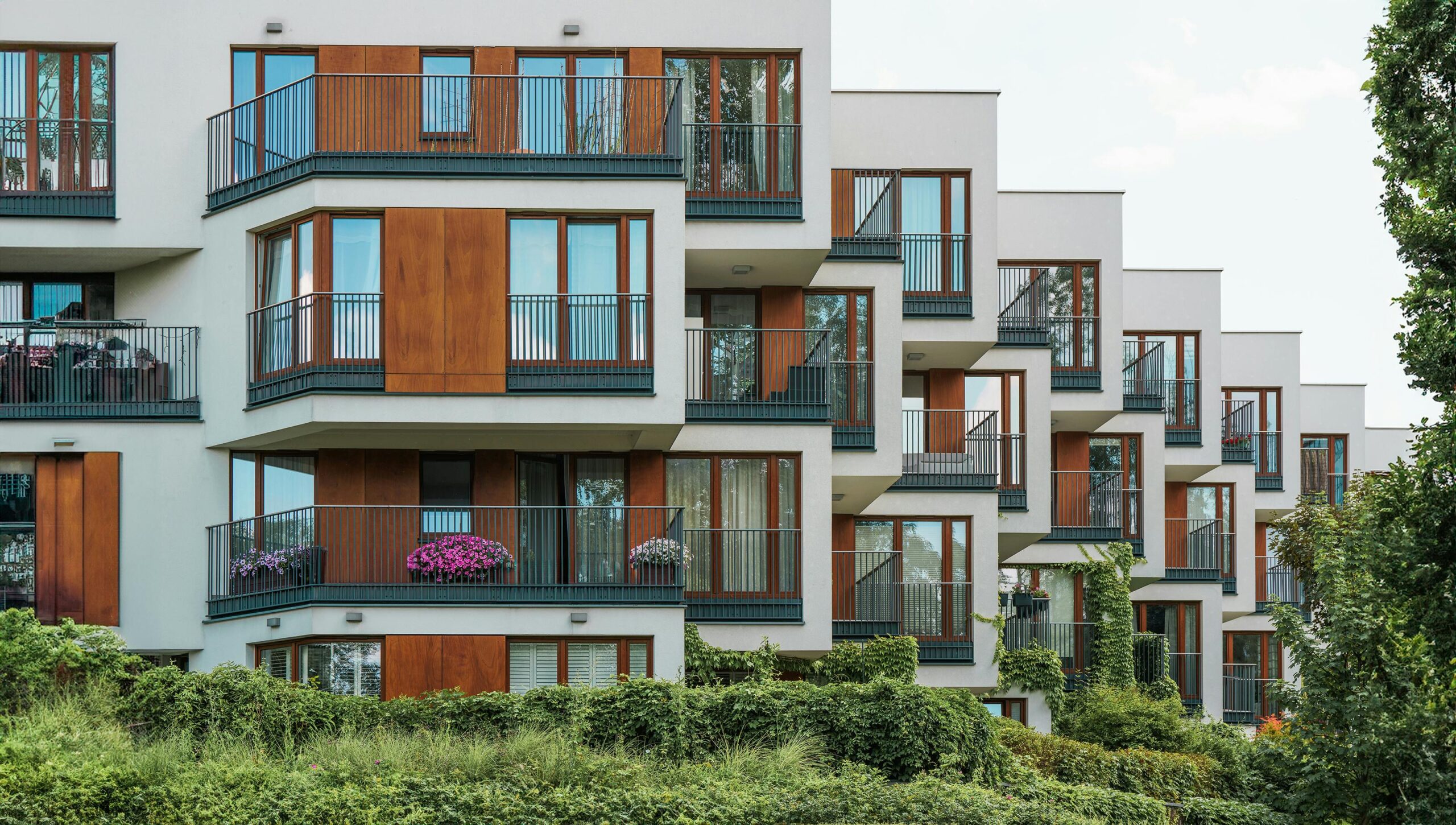 Modern residential building with glass balconies and lush greenery.